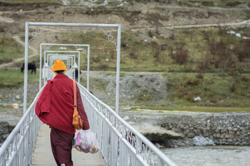 Obraz na płótnie Canvas Tibetan monk, with back to the camera, holding groceries in a plastic bag, crossing a bridge next to the town of Tagong (Lhagang), Kangding, Garzê Tibetan Autonomous Prefecture, Sichuan, China