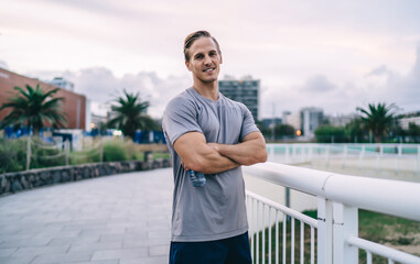 Positive young hipster guy in active wear looking at camera completing cardio workout satisfied with results, portrait of smiling male trainer with crossed arms looking at camera ready for exercising