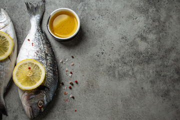Raw fresh fish dorado with lemon wedges, olive oil and seasonings on gray concrete background ready...