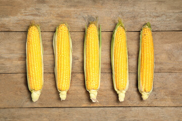 Tasty sweet corn cobs on wooden table, flat lay
