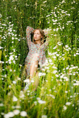 Beautiful blonde girl laying in camomile field outdoor in wild nature. Girl on green grass