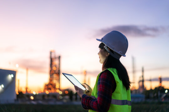 Asian woman petrochemical engineer working at night with digital tablet Inside oil and gas refinery plant industry factory at night for inspector safety quality control..