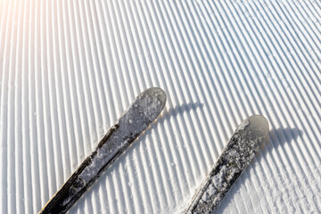 Panorama point of view skier legs on downhill start straight line rows freshly prepared groomed ski slope piste on bright day blue sky background. Snowcapped mountain landscape europe winter resort