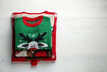 Folded warm Christmas sweaters on white wooden table, top view. Space for text