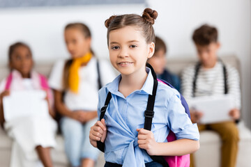 Selective focus of girl with backpack looking at camera in school