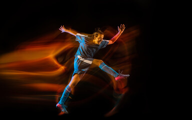 Fototapeta na wymiar Motion. Football or soccer player on black studio background in mixed light. Young male sportive model training in action. Kicking ball, attacking, catching. Concept of sport, competition, winning.