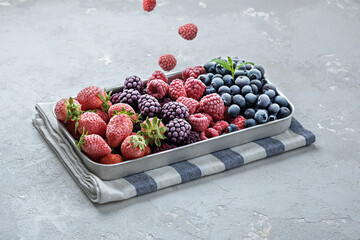 Frozen berries fall into the metal tray on a gray concrete background.