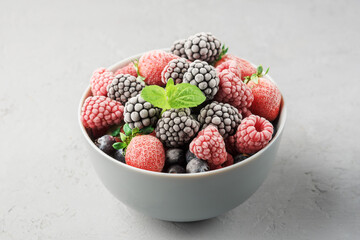 Frozen berries in a grey bowl on a grey concrete background.