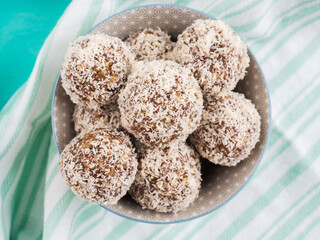 Home made vegan energy protein balls with coconut flakes, almond butter, oats, nuts, dates, dried fruit, flax and hemp seeds served in bowl on turquoise napkin. Top view