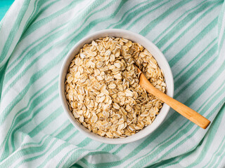 Gluten free oatmeal flakes in white bowl on green turquoise napkin background. Overhead closeup