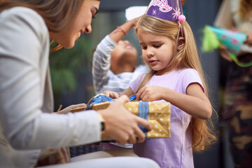 little caucasian girl unwrapping birthday present from young adult female