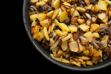 Fried young potatoes with mushrooms and onions. View from above. In a skillet. On a black background.