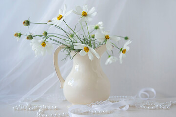 A bouquet of fresh flowers in a light jug in a home interior and threads, ribbons, beads and lace.