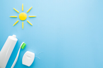 Toothbrush with green bristles, white tube of toothpaste, dental floss on light blue table background. Pastel color. Yellow sun shape. Healthy teeth. Morning routine concept. Top down view.
