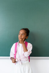 Pensive african american schoolgirl holding backpack near green chalkboard