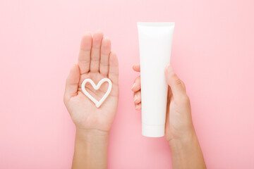 Heart shape created from cream on young woman palm. Hand holding white tube. Point of view shot....