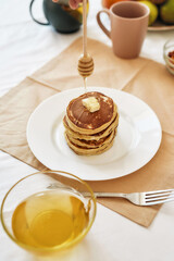 The process of adding honey on top of stack of sweet tasty pancakes on a plate, Process of preparing breakfast on the table