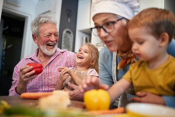 caucasian grandparents having fun with their grandchildren in the kitchen playing