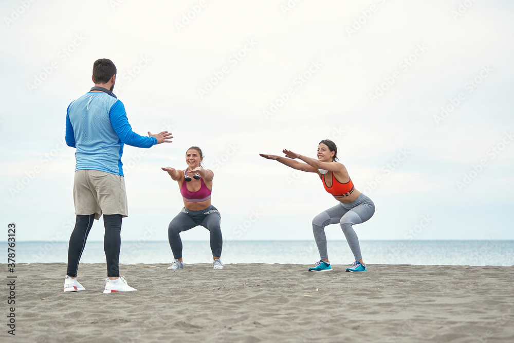 Wall mural Young girls and their trainer having fitness on the beach