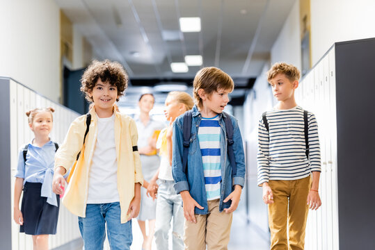 multicultural schoolchildren walking along school corridor with teacher on background