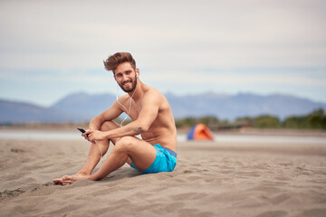 Fototapeta na wymiar Young handsome man sitting on the beach and listening to the music