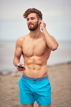 Young handsome man on the beach enjoys music on his smartphone