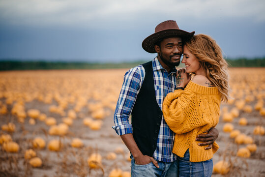 Happy interracial couple in love stands in a pumpkin field. Thanksgiving day concept. Medium shot.