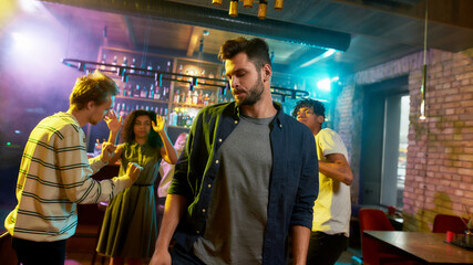 Handsome caucasian young man enjoying evening, celebrating, dancing at party in the bar. People having fun in the background.