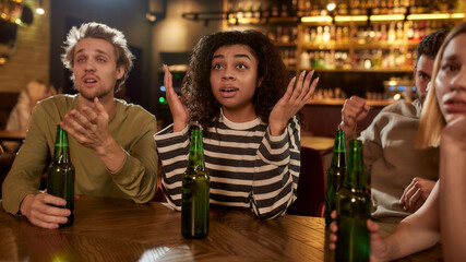 Friends looking disappointed while watching sports match on TV together, drinking beer and cheering for team in the bar. People, leisure, friendship and entertainment concept