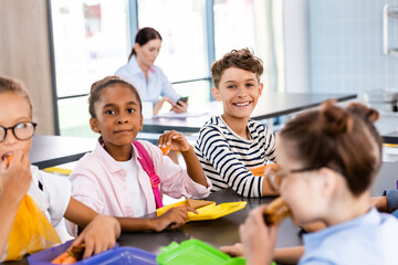 selective focus of multicultural schoolchildren having dinner in school eatery