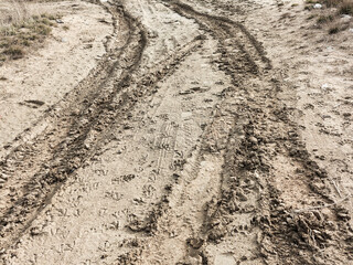 Tyre track and human footprint on sand texture background. Traces of off-road tires. Cracked earth on country road with traces of tires, cars, cracks and dirt. To use as background