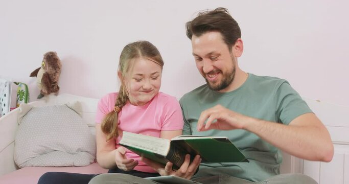 Father and teen daughter are sitting on the sofa, and are looking at the photo album