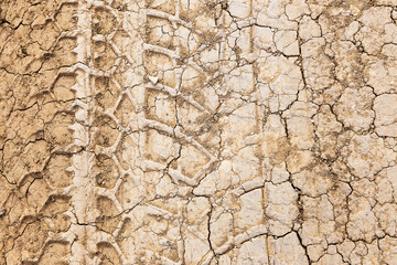 Tyre track and human footprint on sand texture background. Traces of off-road tires. Cracked earth on country road with traces of tires, cars, cracks and dirt. To use as background