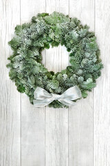 Snow covered spruce fir winter wreath with white bow on rustic wood front door background. Composition for solstice, Christmas & New Year. Copy space.