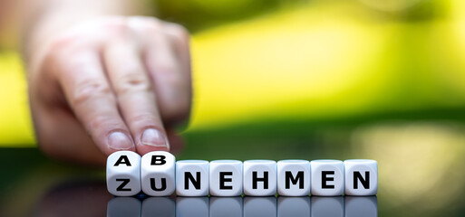 Hand turns dice and changes the German expression "zunehmen" (gain weight) to "abnehmen" (lose weight).
