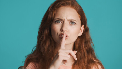 Naklejka premium Angry girl seriously showing silence gesture on camera over colorful background. Don't tell expression