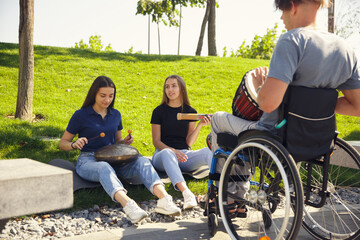 Obraz premium Inspiration. Happy caucasian handicapped man on a wheelchair spending time with friends playing live instrumental music outdoors. Concept of social life, friendship, possibilities, inclusion