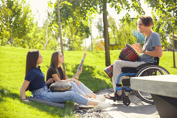 Inspiration. Happy caucasian handicapped man on a wheelchair spending time with friends playing live instrumental music outdoors. Concept of social life, friendship, possibilities, inclusion