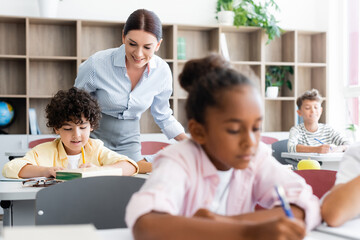 Selective focus of teacher standing beside multicultural pupils in classroom
