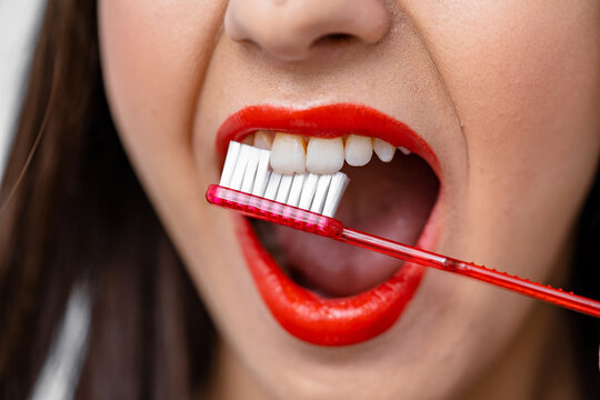Dental concept. Young girl with red lips brushing teeth with toothbrush. Cropped photo.