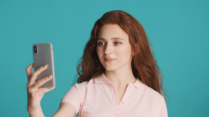 Fototapeta premium Attractive smiling girl talking on video call with friends using smartphone over colorful background