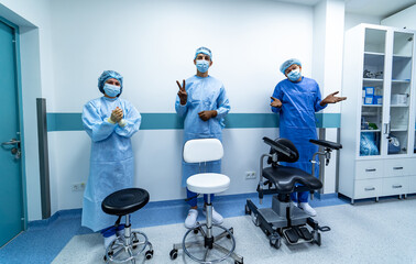 Three office chairs in hospital hall. Three doctors standing behind. Medics in scrubs.