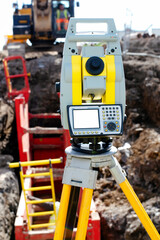 Fototapeta premium Yellow equipment set out on tripod on building site against cloudless blue sky. Construction site surveying engineering equipment, EDM, tacheometer set out on tripod site ready for setting out.