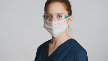 Young professional doctor in protective eyeglasses and medical mask intently looking in camera isolated. Safety first concept