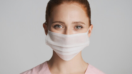 Portrait of female doctor wearing medical mask happily looking in camera over white background. Safety concept