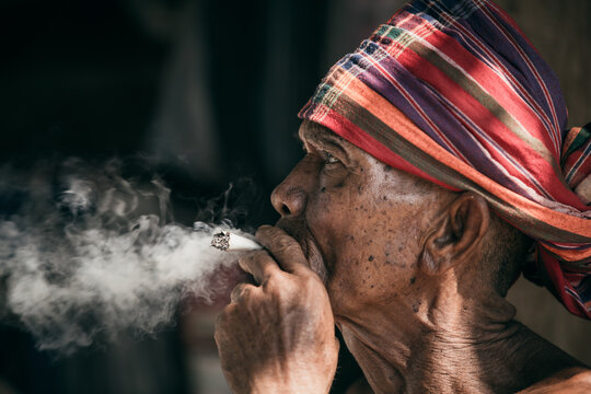 Countryside, old man sitting smoking. Dark background, close up portrait, Thailand.