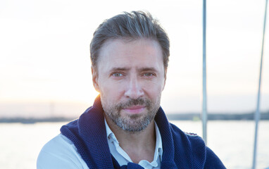 Handsome good-looking mature man on the yacht. Portrait of smiling man on sailing boat at sunset.