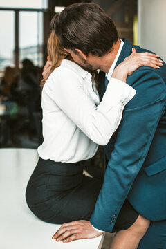 An office worker sits on a desk while a colleague kisses her neck. Passionate affair in the office workplace concept. High quality photo.