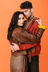 trendy couple in leather jackets hugging isolated on orange