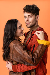 young brunette woman hugging stylish man in jacket isolated on orange